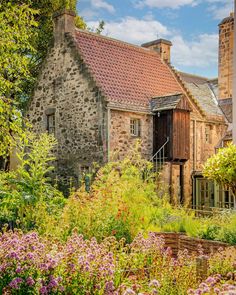 an old stone building surrounded by lots of flowers and greenery in the foreground