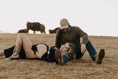 a man and woman laying on the ground with cows in the background