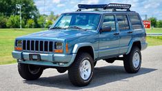 a blue jeep is parked on the side of the road in front of a field