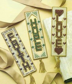 three cross stitch bookmarks with tassels and ribbons around them on a table