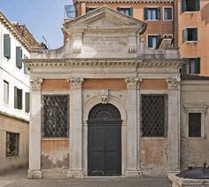 an old building with a black door in front of it and some buildings around it