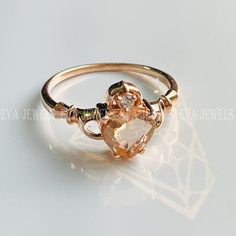 a gold ring with a heart shaped stone on the front and side, sitting on a white surface