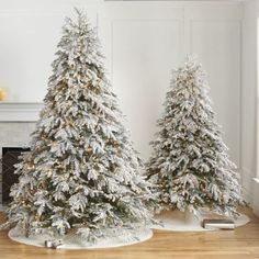 two white christmas trees sitting on top of a hard wood floor next to a fireplace