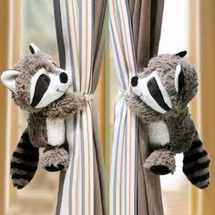 a raccoon stuffed animal hanging from the side of a curtain with striped curtains behind it