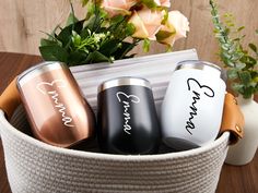 three personalized can coolers sitting in a basket next to a vase with flowers