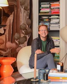 a man sitting on a couch in front of a book shelf filled with books and candles