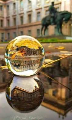 a glass ball sitting on top of a table in front of a building with a horse statue behind it