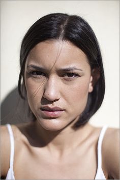 a woman in white shirt looking at the camera with serious look on her face and shoulder