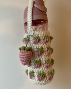 a crocheted strawberries bag hanging from a hook on a chain with a bottle in the background