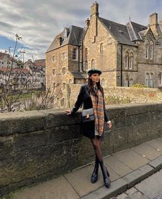 a woman standing on the side of a road next to a stone wall with buildings in the background