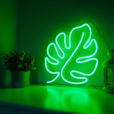 a green neon sign sitting on top of a table next to a potted plant