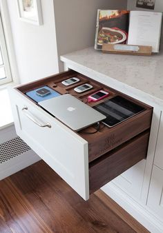 an open drawer on the side of a desk with various electronics and books in it