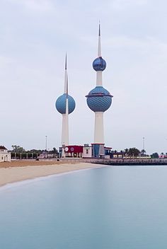 two blue and white towers in the middle of a body of water next to buildings