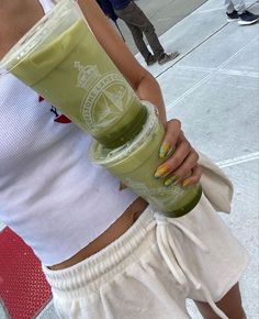 a woman holding a green smoothie in her right hand and a drink in the other