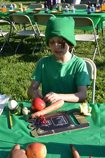 a young boy wearing a green hat sitting at a table with apples and carrots