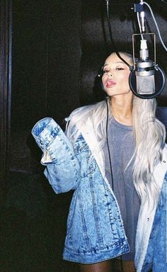 a woman standing in front of a microphone with headphones on her ears and wearing a jean jacket