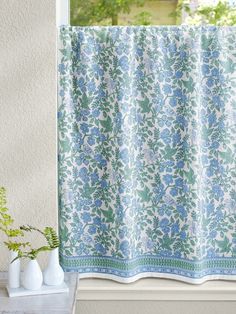 a blue and white floral curtain hanging on a window sill next to a vase with flowers