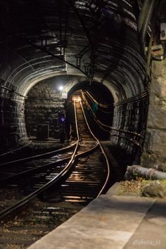 a train track going into a tunnel with lights at the end and some tracks running through it