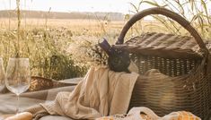 a picnic basket with bread, wine glass and napkins on the table in front of an open field