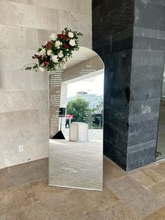 a vase with flowers sitting in front of a large mirror on the floor next to a wall