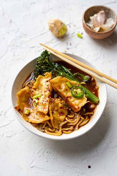 a bowl filled with noodles, broccoli and other vegetables next to chopsticks