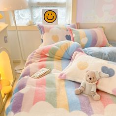 a teddy bear is laying on a bed with colorful sheets and pillows in front of a window