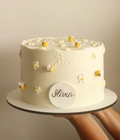 a person holding a white cake with yellow flowers on it