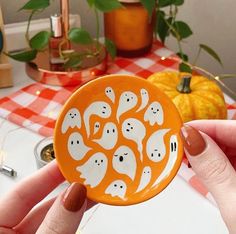 a person holding an orange button with white ghost faces on it and pumpkins in the background