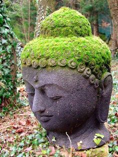 a statue with moss growing on it's head in the woods