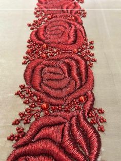 an embroidered table runner with red beads and flowers on the edge, in front of a white background