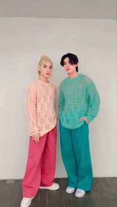 two people standing next to each other in front of a white wall wearing colorful clothing