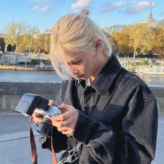 a woman is looking at her cellphone while standing on the sidewalk in front of some water