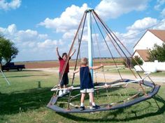 two children are playing on a homemade sailboat in the grass with their arms up