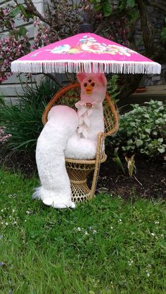 a stuffed animal sitting on top of a chair under an umbrella in the grass next to flowers