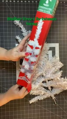 someone is holding a red and white christmas cracker in front of a fake tree