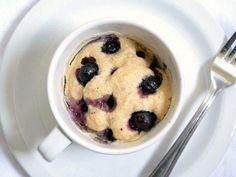 a white plate topped with a bowl of blueberry muffins next to a fork