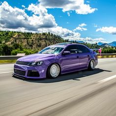 a purple car is driving down the road with mountains in the background and clouds in the sky