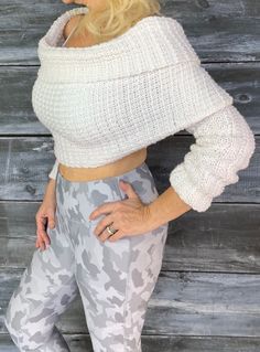 a woman wearing grey camouflage print leggings and a white cropped sweater is posing in front of a wooden wall