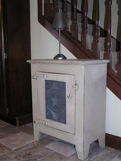 a small cabinet with a lamp on top of it in front of a stair case