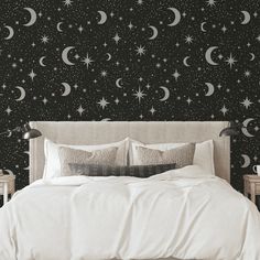 a bed sitting under a night sky with stars and crescents on the wall behind it