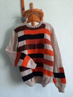 an orange and black striped sweater hanging on a wooden hanger next to a white wall