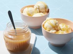 three bowls filled with ice cream on top of a blue countertop next to a jar of caramel sauce