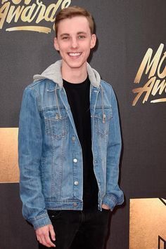 a young man standing on top of a red carpet wearing black pants and a jean jacket