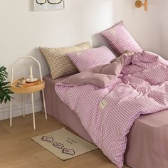 a bed with pink comforter and pillows in a white room next to a potted plant