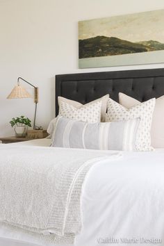 a bed with white linens and pillows in a small room next to a painting on the wall