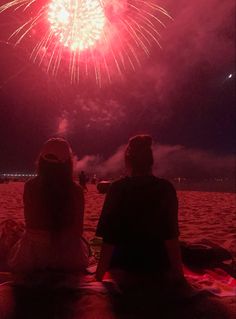 two people sitting on the beach watching fireworks