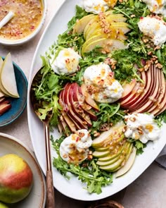 a white plate topped with an apple salad next to bowls of fruit and dips