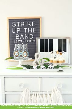 a white dresser topped with cupcakes next to a sign that says strike up the band let's party