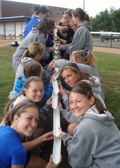 a group of young women standing next to each other in front of a baseball field