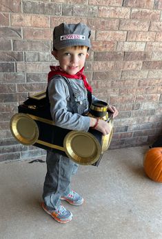 a young boy dressed up as a car with a hat and scarf on, holding a coffee cup in his hand